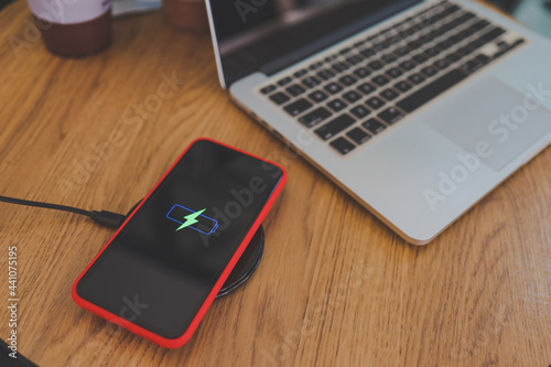 Charging mobile phone battery with wireless device in the table. Smartphone charging on a charging pad. Mobile phone near wireless charger.