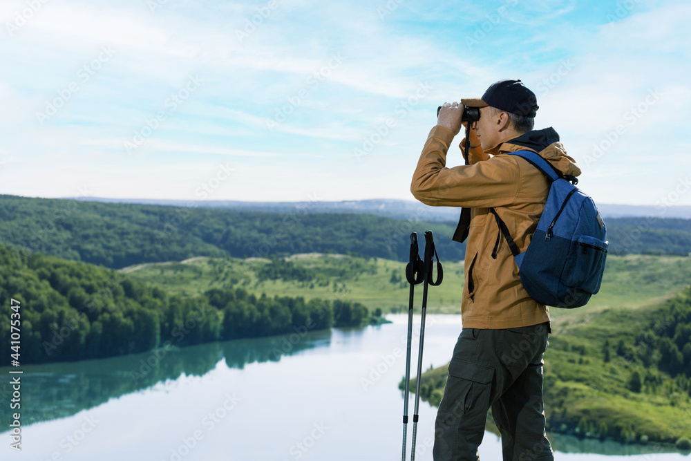 Hiker man looking in binoculars on the mountain. Hiking active people lifestyle. - obrazy, fototapety, plakaty 