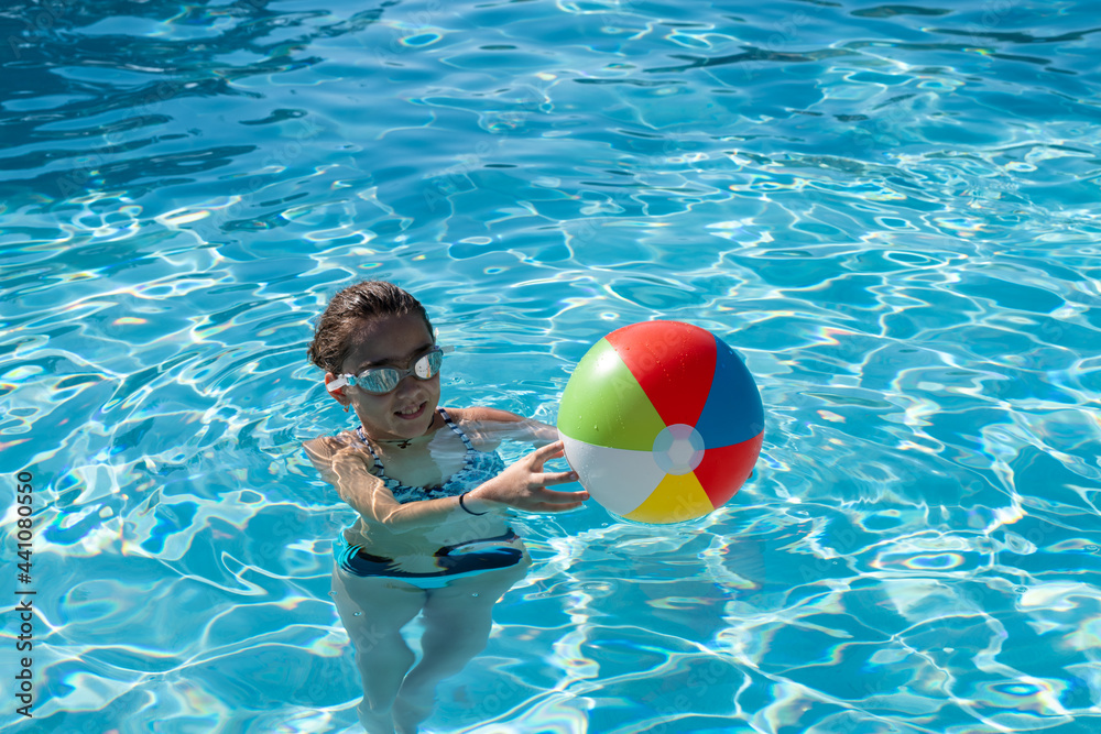 Young girl playing with beach ball in the swimming pool. Kid outdoor activities. Summer concept. Happy childhood.