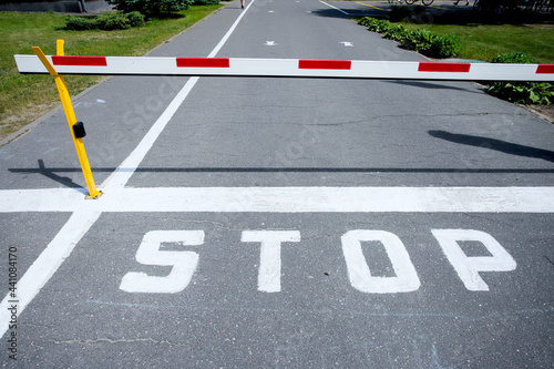 A barrier and the STOP sign on the road. White-red barrier on the road. Green along the edges of the road. High quality photo