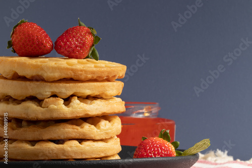 A pile of waffles served with strawberries and jelly.