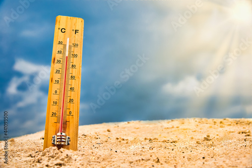 Weather thermometer in the sand against the sky showing a high ambient temperature photo