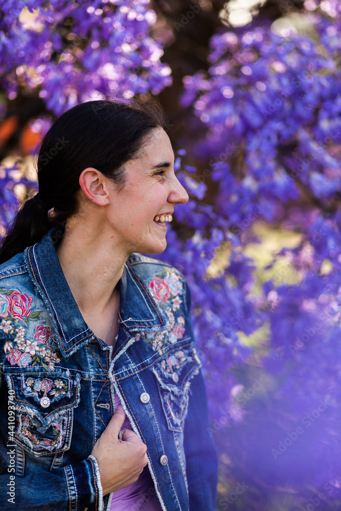 Side on profile of happy woman laughing in spring with background of purple jacaranda flowers