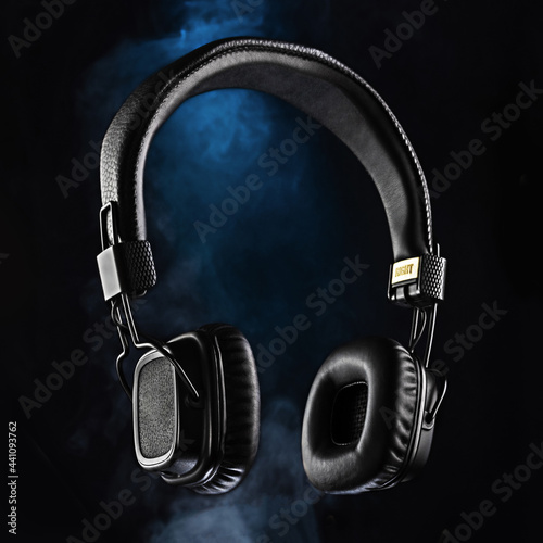 Audio headphones on a black background. Black headphones and blue smoke. Advertising photo of headphones.