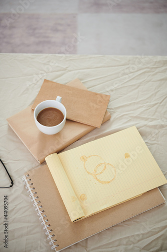 Opened notepad with coffee stains, books, planners and cup with cappuccino on bed