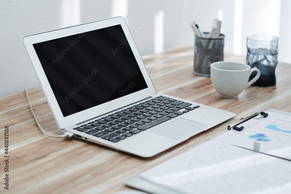Opened laptop with empty screen and sales reports with charts and diagrams on table of product manager Opened laptop with empty screen and sales reports with charts and diagrams on table of product manager