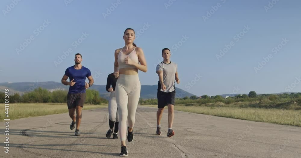 Multiethnic group of athletes running together on a panoramic countryside road. Diverse Team of joggers on morning training. Multiethnic group of athletes running together on a panoramic countryside road. Diverse Team of joggers on morning training.
