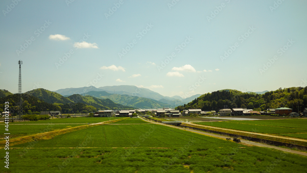 Panoramic view of a meadow of rural area in Japan. Houses in village in background. Clouds in blue sky. No people.