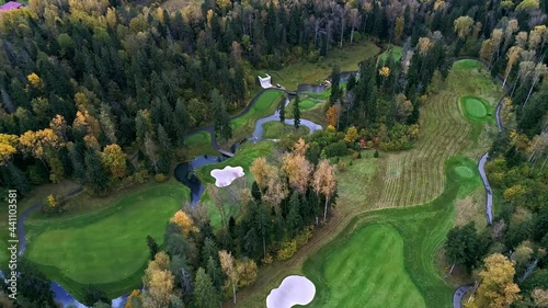 Aerial view of Golf course near the forest. Establishing shot, drone flying over country golf club. Autumn, cloudy. Beautiful prestigious green golf course with river and trees. Drone areal view shot
