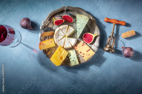 Cheese platter with wine and fruit, shot from the top on a blue background with a place for text. Different cheeses and a glass of red wine