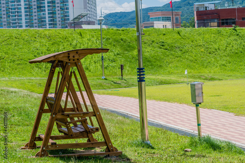 Wooden swing park bench beside walkway with city buildings in background.