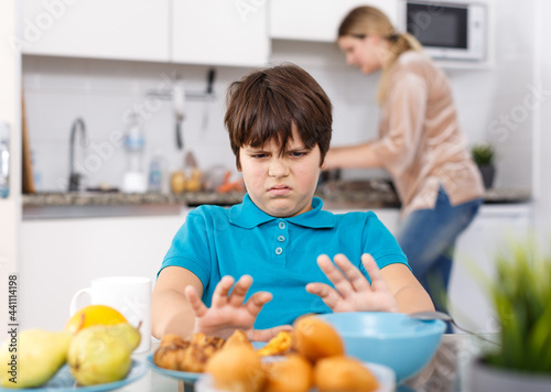 Portrait of school age boy sitting at kitchen table do not want to eat