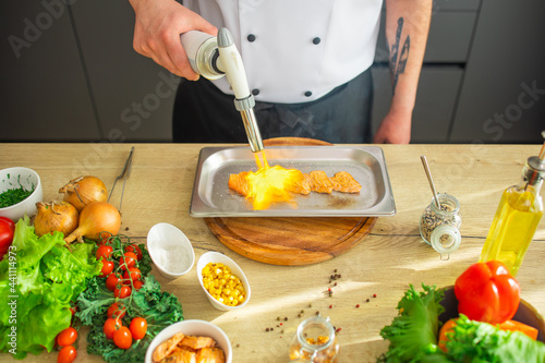 Young chef fries salmon fish with a gas burner in a modern kitchen. The man prepares food at home. Cooking healthy and tasty food.