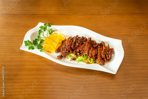 Tray of roasted orange chicken sliced into fillets with garnishes of lettuce, parsley and orange slices on wooden table