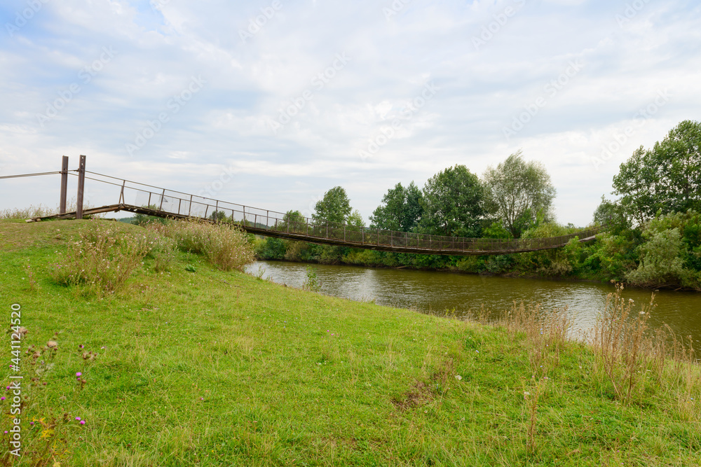 Fototapeta premium Old suspension bridge over the river on a cloudy summer day