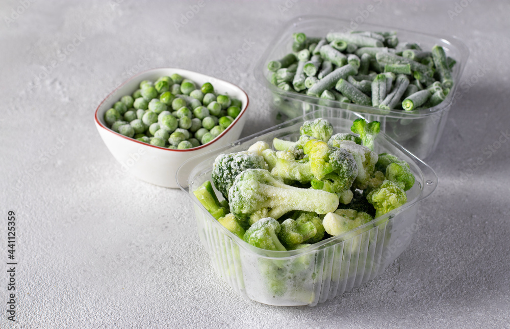 Frozen vegetables such as green peas, green beans and broccoli in the storage boxes on the light gray background. Frozen vegetables such as green peas, green beans and broccoli in the storage boxes on the light gray background.