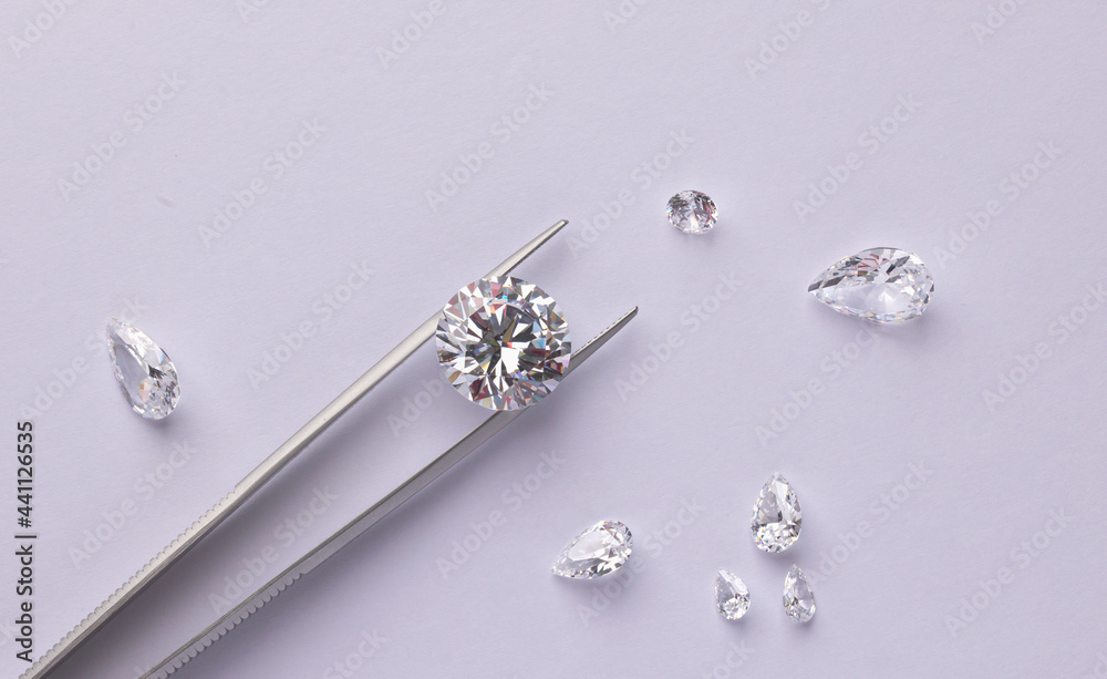Polished diamonds of various sizes and shapes wit jewelry tools lie at the workplace of an expert examining the quality of stones on light background with copy space. High quality photo
