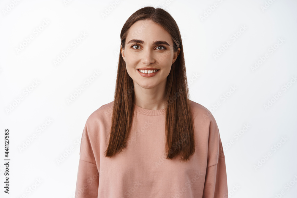 Close up portrait of brunette girl smiling happy, white teeth, looking carefree at camera, standing in pink sweatshirt, casual relaxed pose, white background Close up portrait of brunette girl smiling happy, white teeth, looking carefree at camera, standing in pink sweatshirt, casual relaxed pose, white background