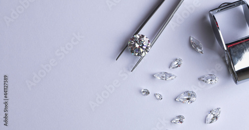 Polished diamonds of various sizes and shapes wit jewelry tools lie at the workplace of an expert examining the quality of stones on light background with copy space. High quality photo