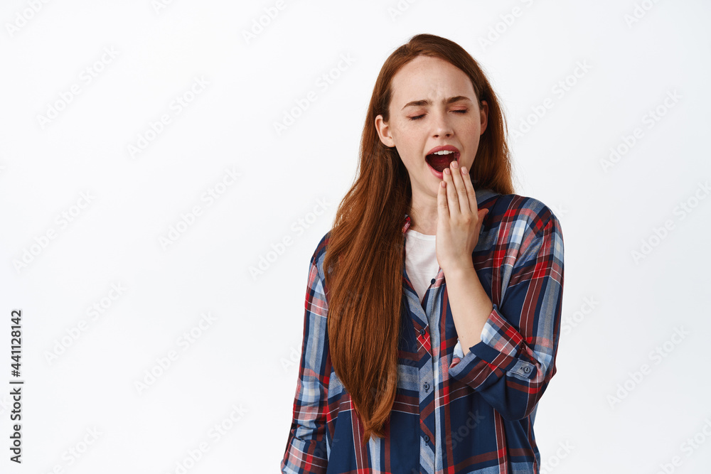 Image of tired redhead girl yawning, looking tired or bored, feeling boredom and reluctance, yawn with opened mouth, standing against white background Image of tired redhead girl yawning, looking tired or bored, feeling boredom and reluctance, yawn with opened mouth, standing against white background