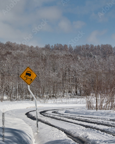 Yellow slippery road sign and snowy road, Hokkaido, Japan