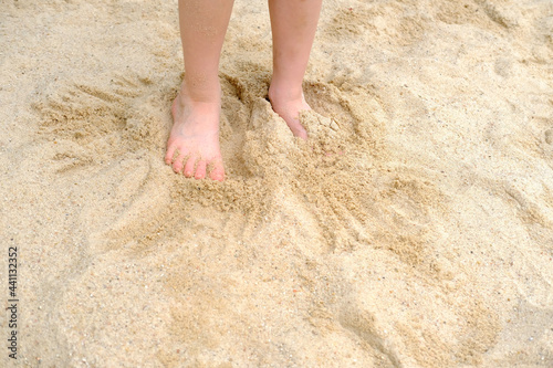 child's bare feet in the sand, boy plays in the summer with sand on the playground, in the sandbox, the concept of building sand castles, summer vacation, fun on the beach