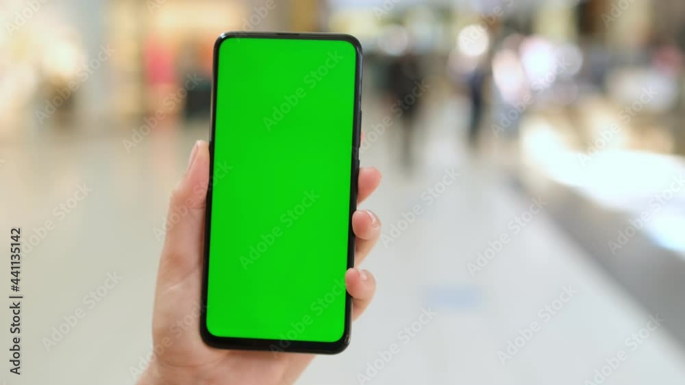 Mall. Shopping center. Back view of brunette holding chroma key green screen smartphone watching content. Shopping online. Gadgets and contemporary people concept. Mall. Shopping center. Back view of brunette holding chroma key green screen smartphone watching content. Shopping online. Gadgets and contemporary people concept.