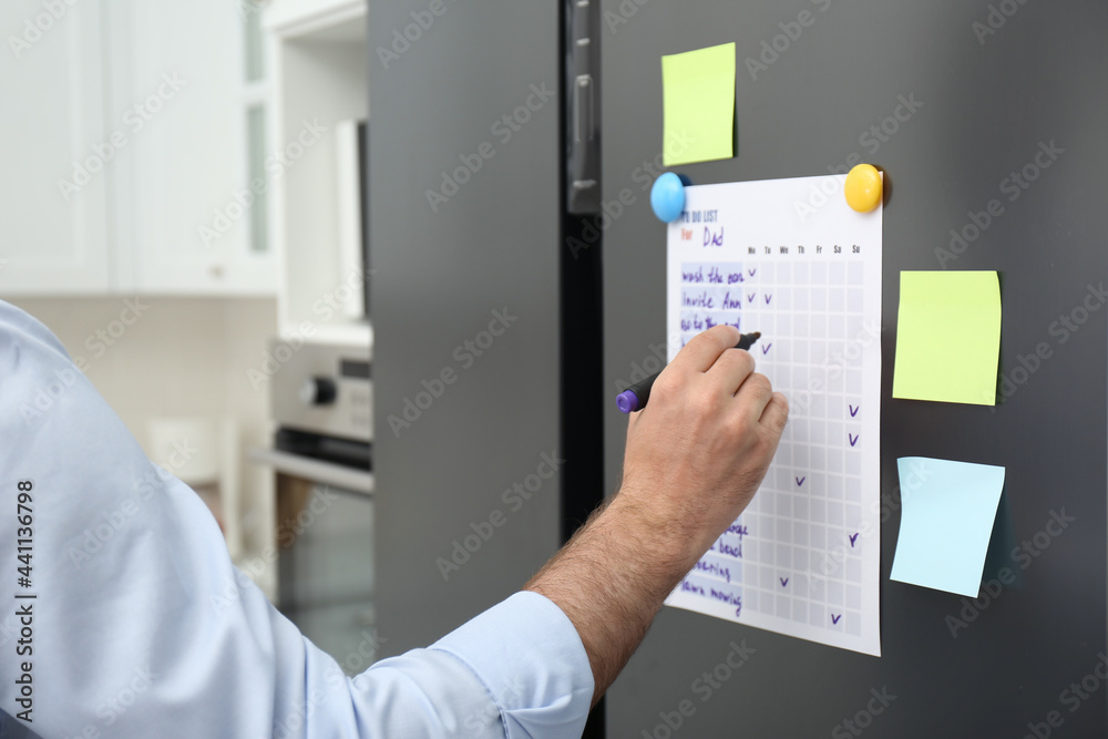 Man checking to do list on fridge in kitchen, closeup - obrazy, fototapety, plakaty 