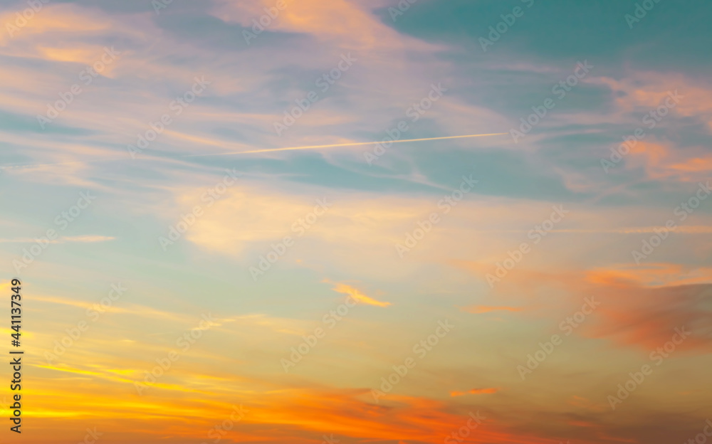 Sunset sky with condensation trail. Texture of bright evening sky during sunset. Dramatic blue and orange, colorful clouds at twilight time. Abstract weather nature background.