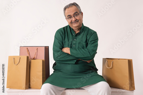 AN OLD MAN LOOKING AT CAMERA WHILE SITTING WITH SHOPPING BAGS photo