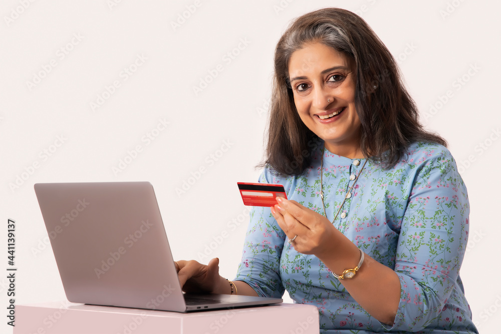 A SENIOR ADULT WOMAN LOOKING AT CAMERA WHILE DOING ONLINE TRANSACTIONS A SENIOR ADULT WOMAN LOOKING AT CAMERA WHILE DOING ONLINE TRANSACTIONS