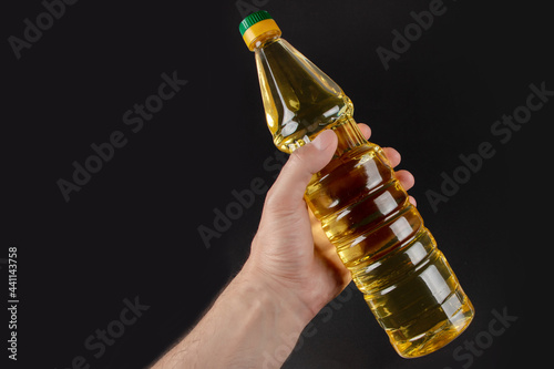 Hand with bottle of cooking oil on blsck background