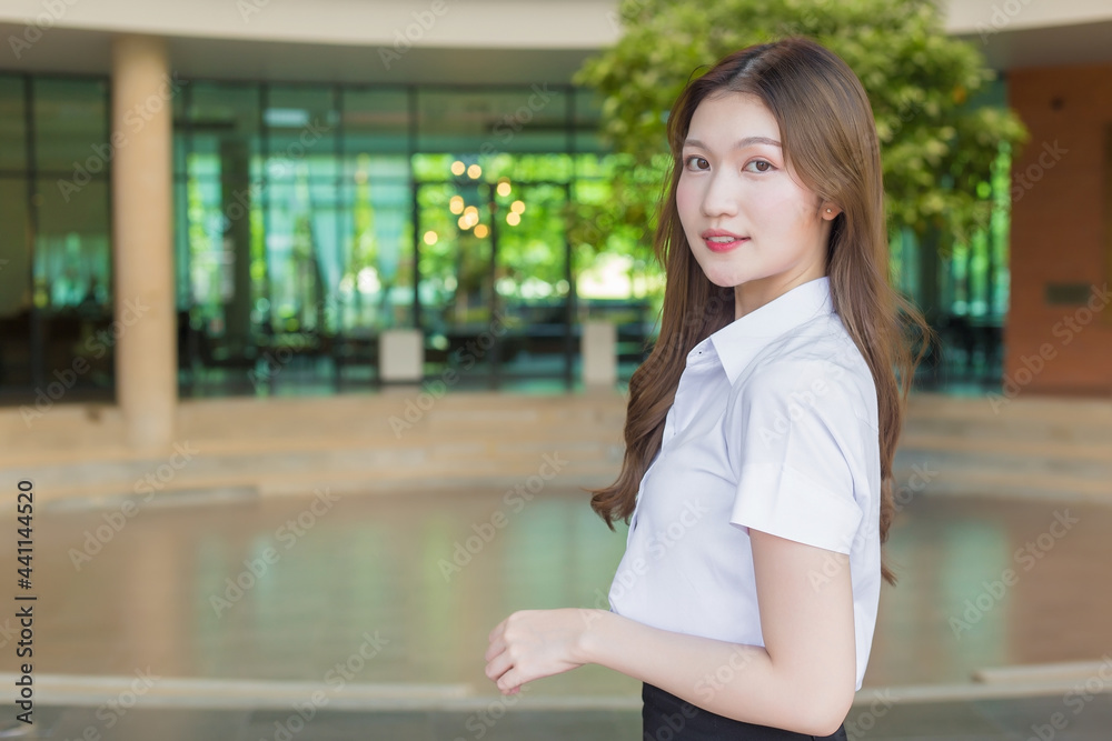 Portrait of an adult Thai student in university student uniform. Asian beautiful girl standing smiling happily at university