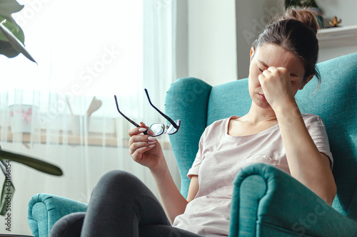 Young woman with glasses in hands sits in a chair and suffers fr