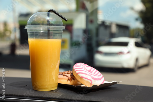 Fototapeta Naklejka Na Ścianę i Meble -  Plastic cup of juice and doughnuts on car dashboard at gas station. Space for text