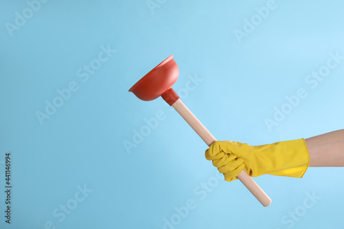 Woman holding plunger on turquoise background, closeup. Space for text photo