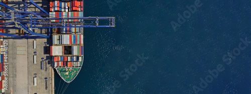 Aerial top down ultra wide photo of industrial container ship loading  - unloading colourful truck size containers with cranes in logistics terminal port