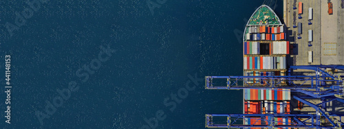 Aerial top down ultra wide photo of industrial container ship loading  - unloading colourful truck size containers with cranes in logistics terminal port