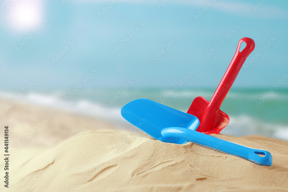 Red and blue plastic toy shovels on sandy beach near sea, space for text Red and blue plastic toy shovels on sandy beach near sea, space for text