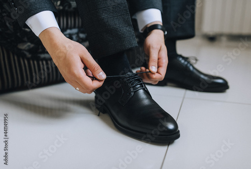 A man, a businessman, a groom ties long shoelaces on black leather shoes, shiny with cream, with his hands in a jacket close-up. Photography, concept.
