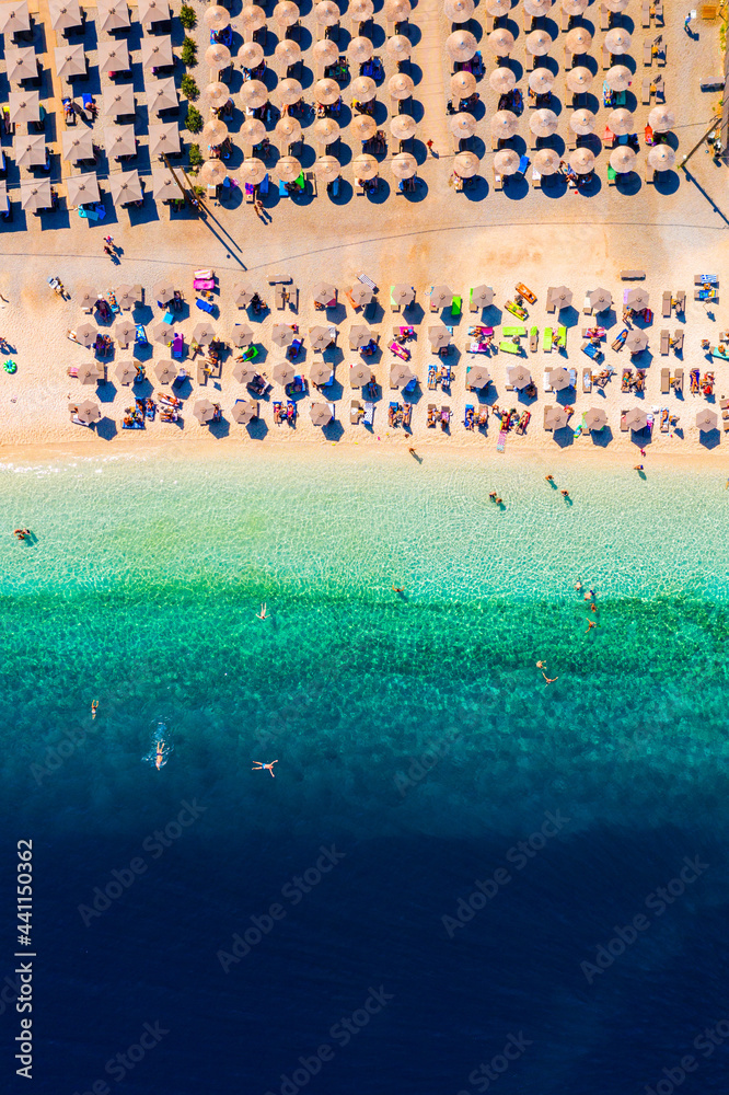 View from above, stunning aerial view of an amazing beach with beach umbrellas and turquoise clear water. Top view on sun loungers under umbrellas on the sandy beach. Concept of summer vacation.