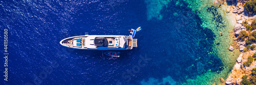 Fototapeta Naklejka Na Ścianę i Meble -  Aerial view of anchored sailing yacht in emerald sea. Aerial view of a boat. Outdoor water sports, yachting. Aerial view of anchoring yacht in open water. Ocean and sea travel and transportation