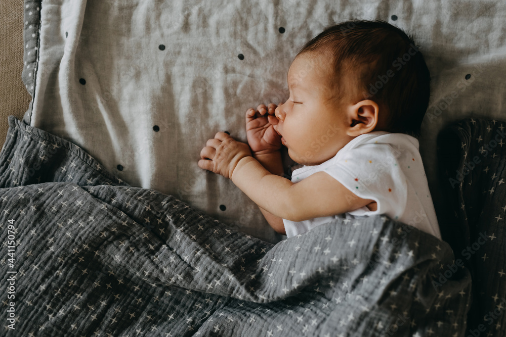 Newborn baby sleeping on her side, covered with a grey blanket. Stock