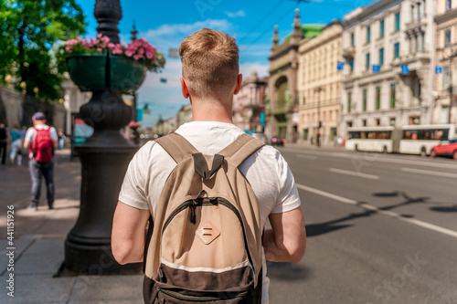 A young man with a blonde hair and a backpack walks in the center of the street in St. Petersburg in the summer