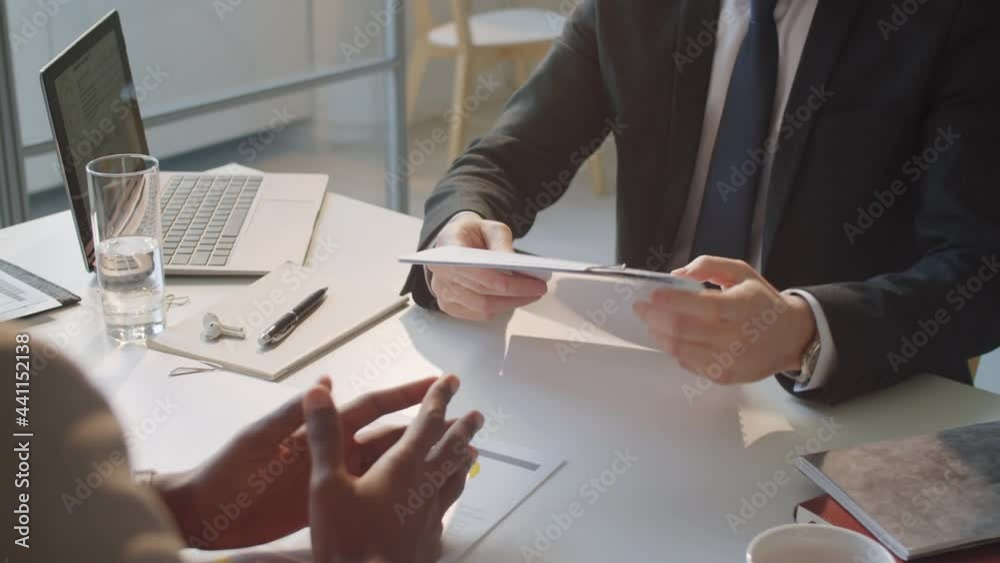 Close up over the shoulder shot of Afro-American businessman giving contract to Caucasian partner and shaking hands with him after signing