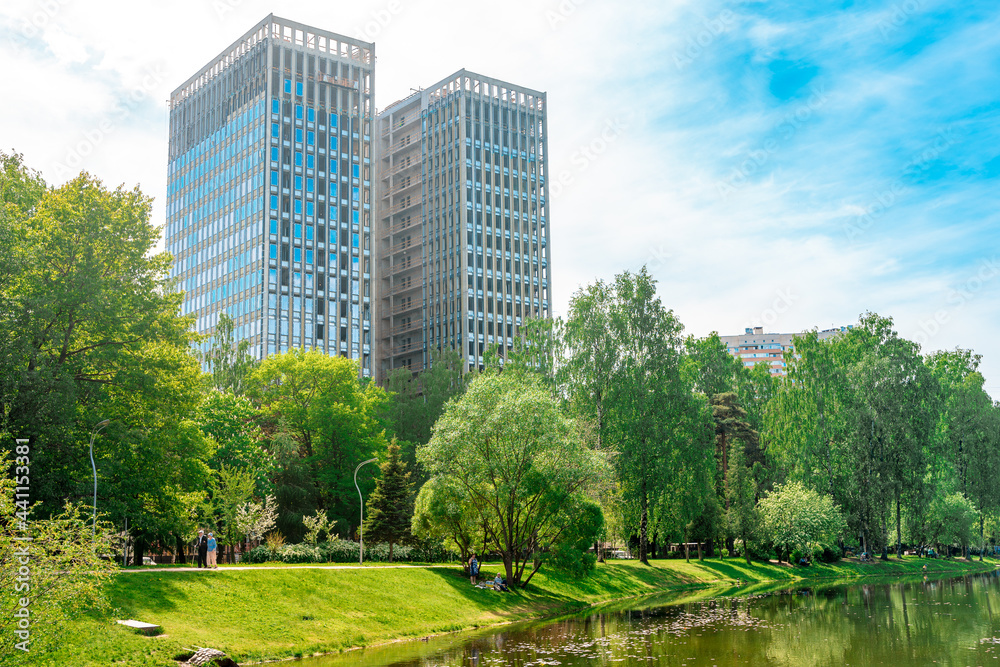 Beautiful green park with a pond in the center of the city with a residential high-rise in saint petersburg