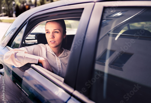 Serious woman in car. Sad, upset or tired taxi passenger. Cool elegant business lady sitting on the back seat looking out the window. Commuter late, waiting in traffic. Thoughtful female cab customer. © terovesalainen