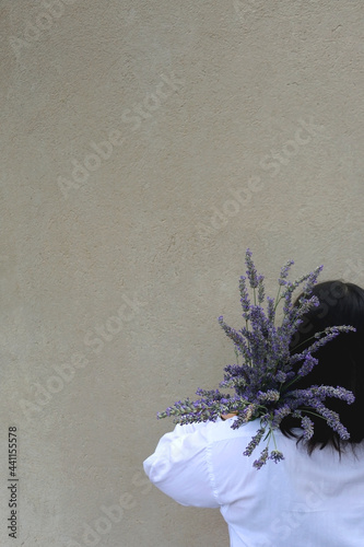 Unrecognizable person holding a bouquet of lavender flowers. Selective focus, simple concrete background.