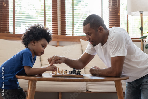 Brazilian Father and little boy playing chess on table at home together. Happy Black African American Family engaged in board game on holiday.
