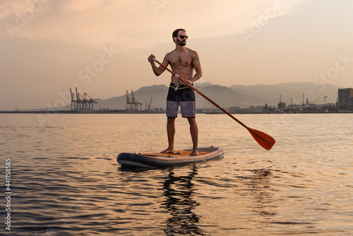 Photography Young man paddle surfs in the sea at sunset